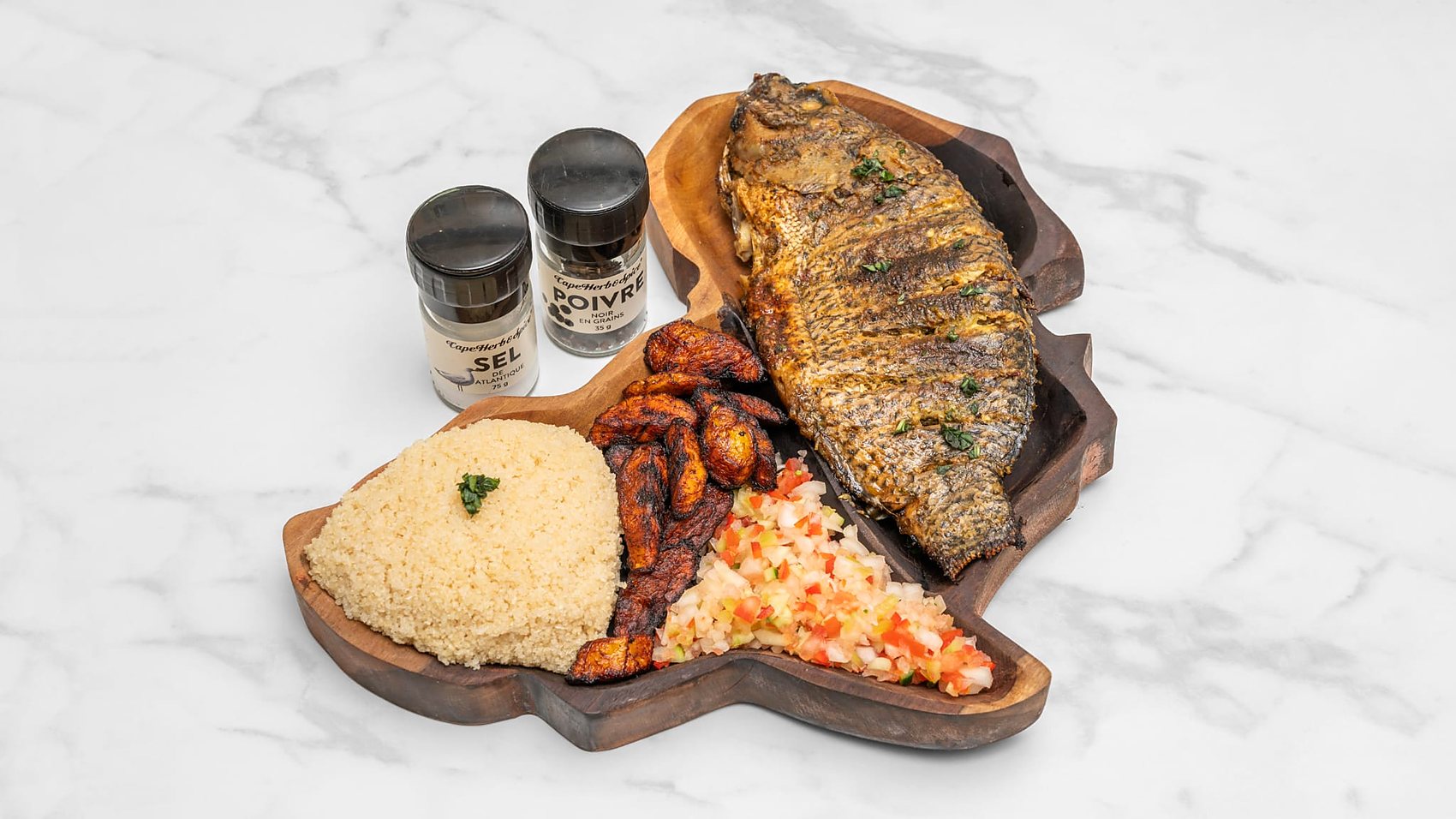 Poisson braisé entier, attiéké, plantains et salsa sur planche en forme d'Afrique
