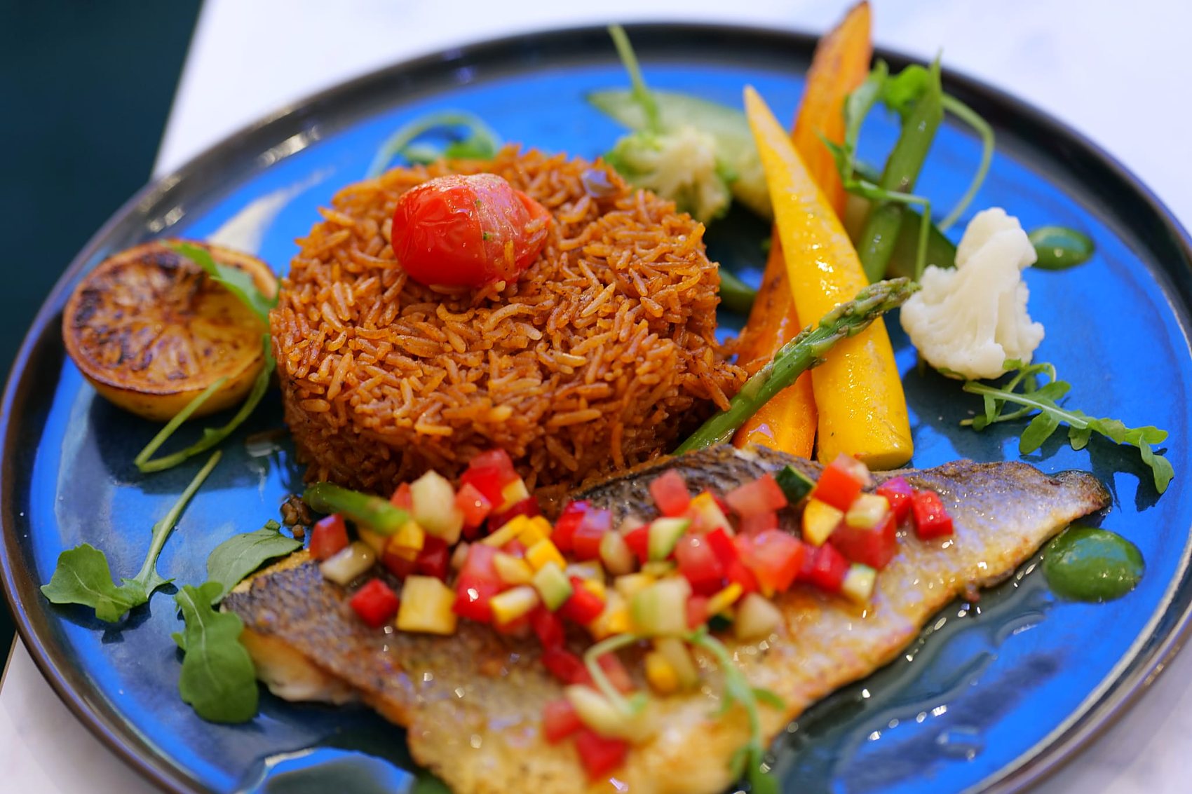 Riz jollof et filet de dorade servis sur une assiette bleue méditerranéenne
